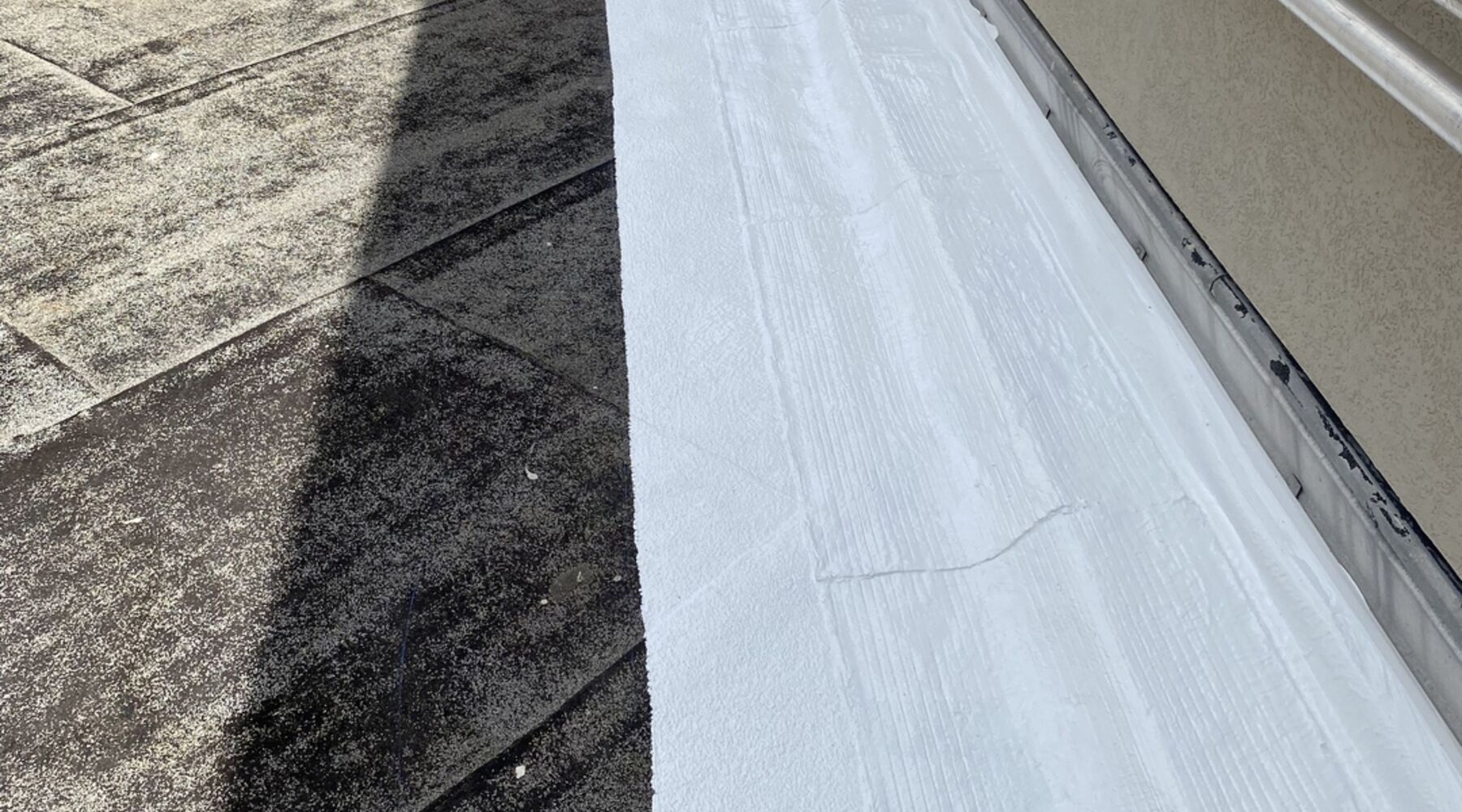 Freshly applied white waterproof coating along a commercial rooftop parapet seam in South Florida